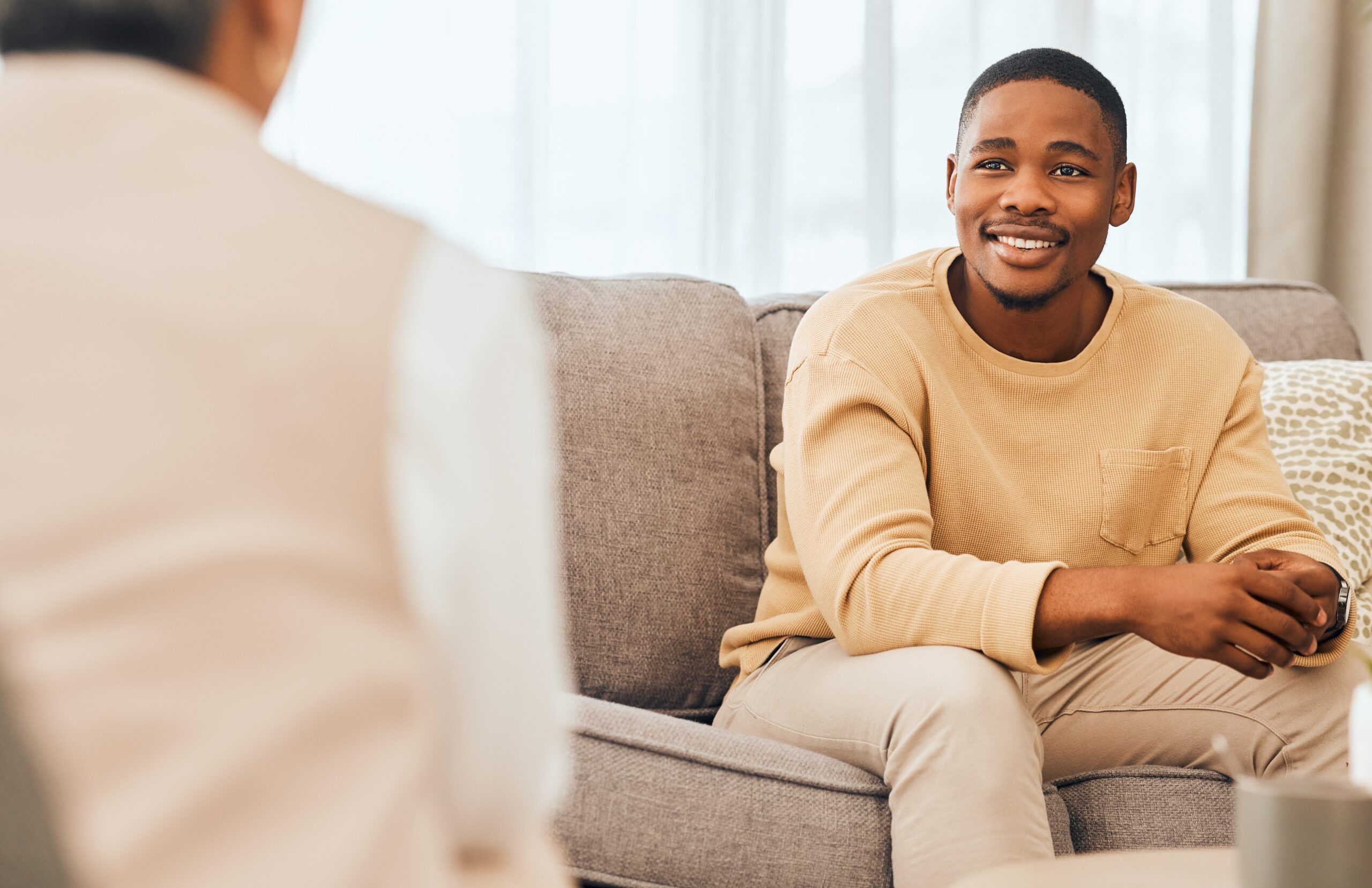 man sitting on a couch in therapy smiling because he is navigating mental health treatment with positive outcomes